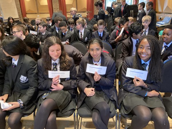Groups of students sat in rows girls on front row holding cheques after a business talk