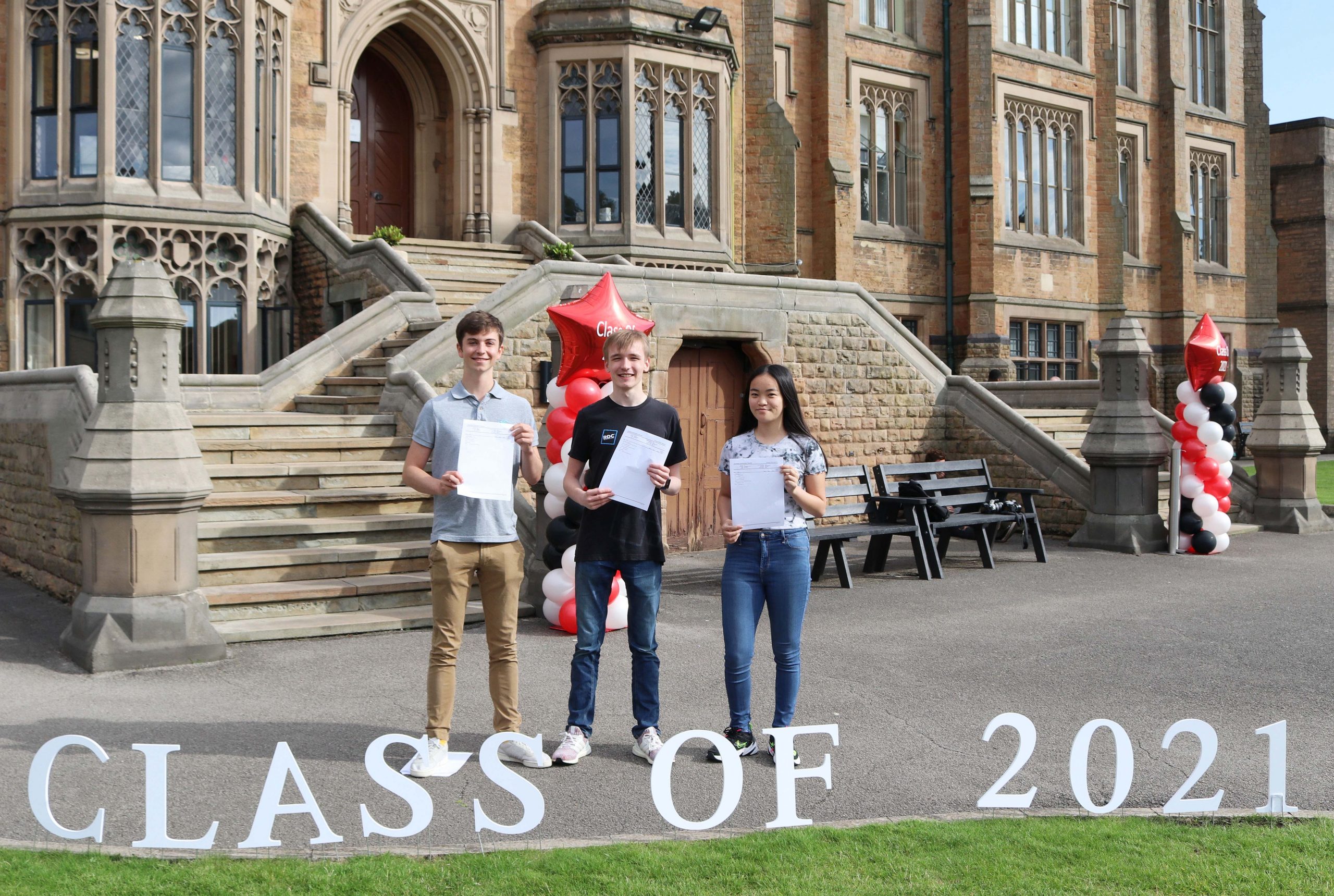 3 Students holding A Level results in front of Class of 2021 sign 