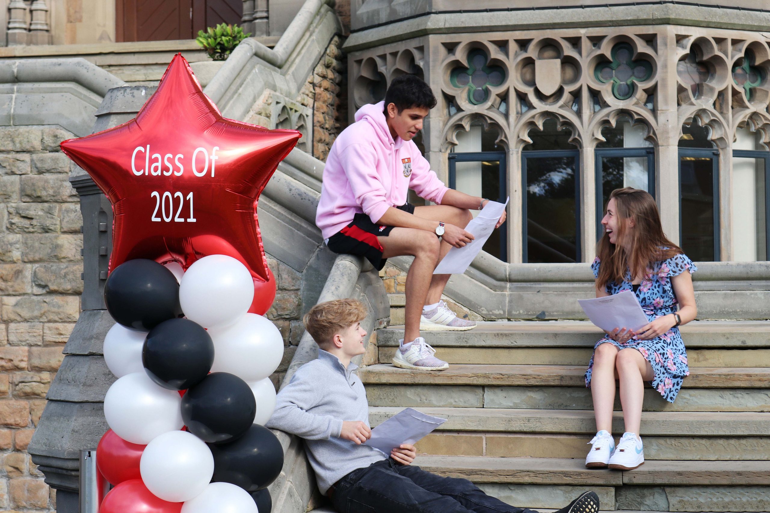 3 Students sat on steps reading their A Level results