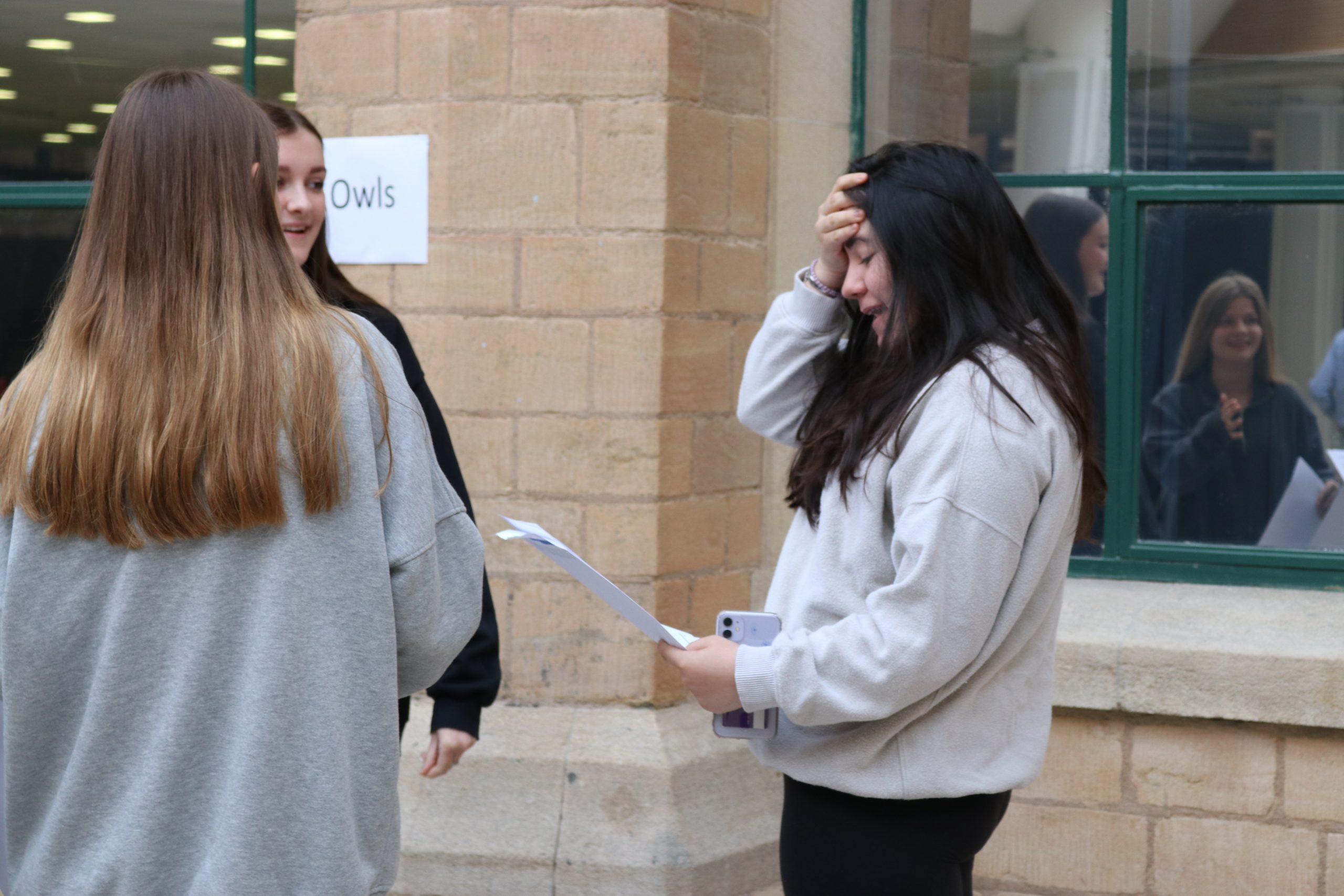 Girl stood with two friends smiling with surprised look after receiving her GCSE results 
