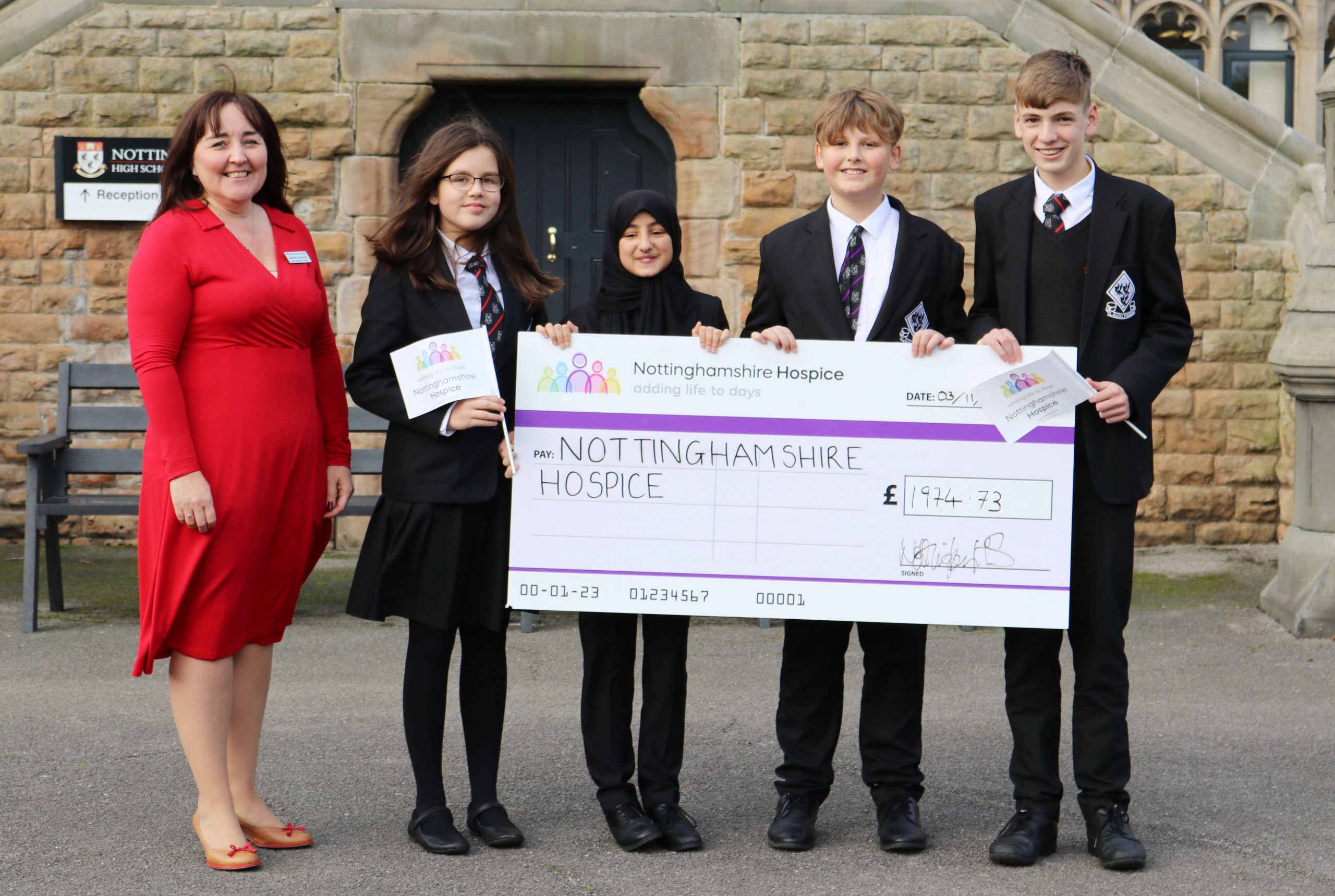 Group of Students holding a giant cheque next to lady in red dress